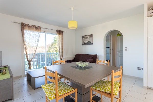 Un coin repas avec une table en bois, des chaises, une suspension jaune et une vue sur l’extérieur.