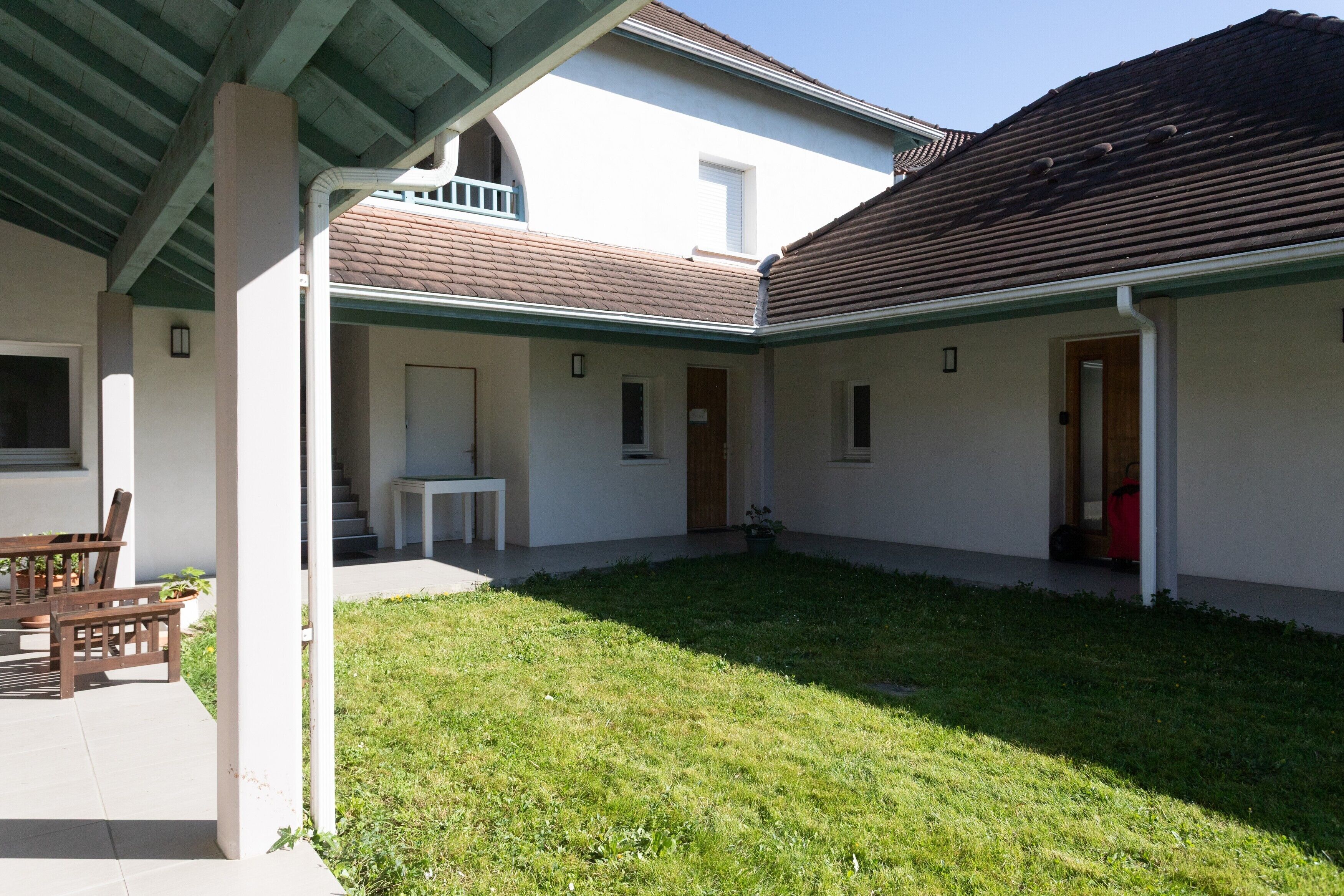 A covered outdoor area with a lawn, a table with chairs, and a door leading to a building.