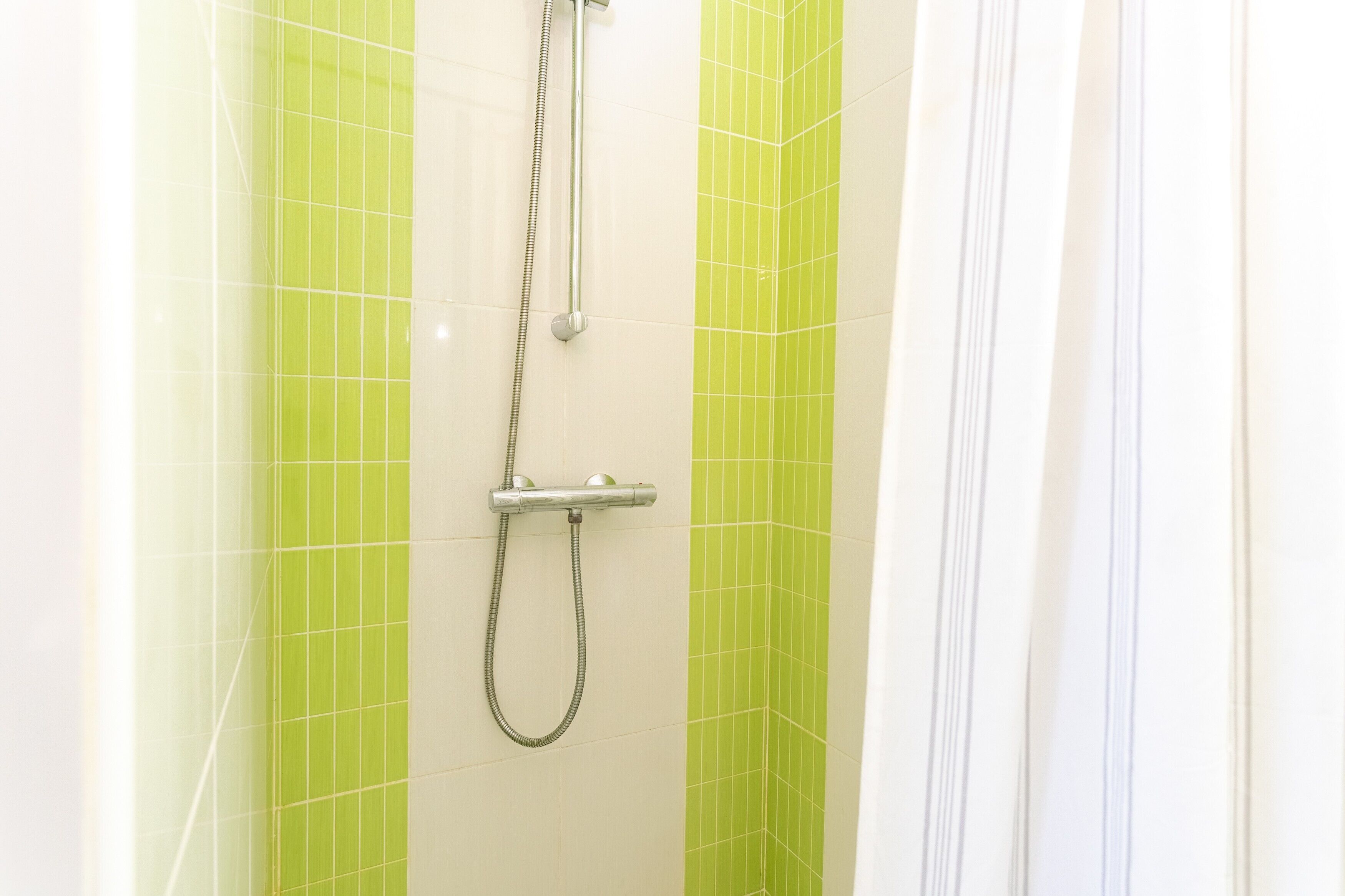 Een douche met een handdouche en een bediening aan de muur.