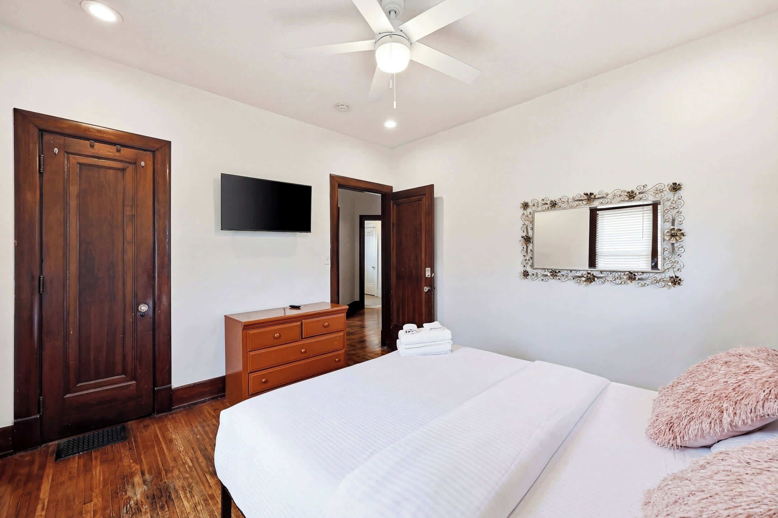 Un dormitorio con una cama, un aparador, un espejo y un ventilador de techo.