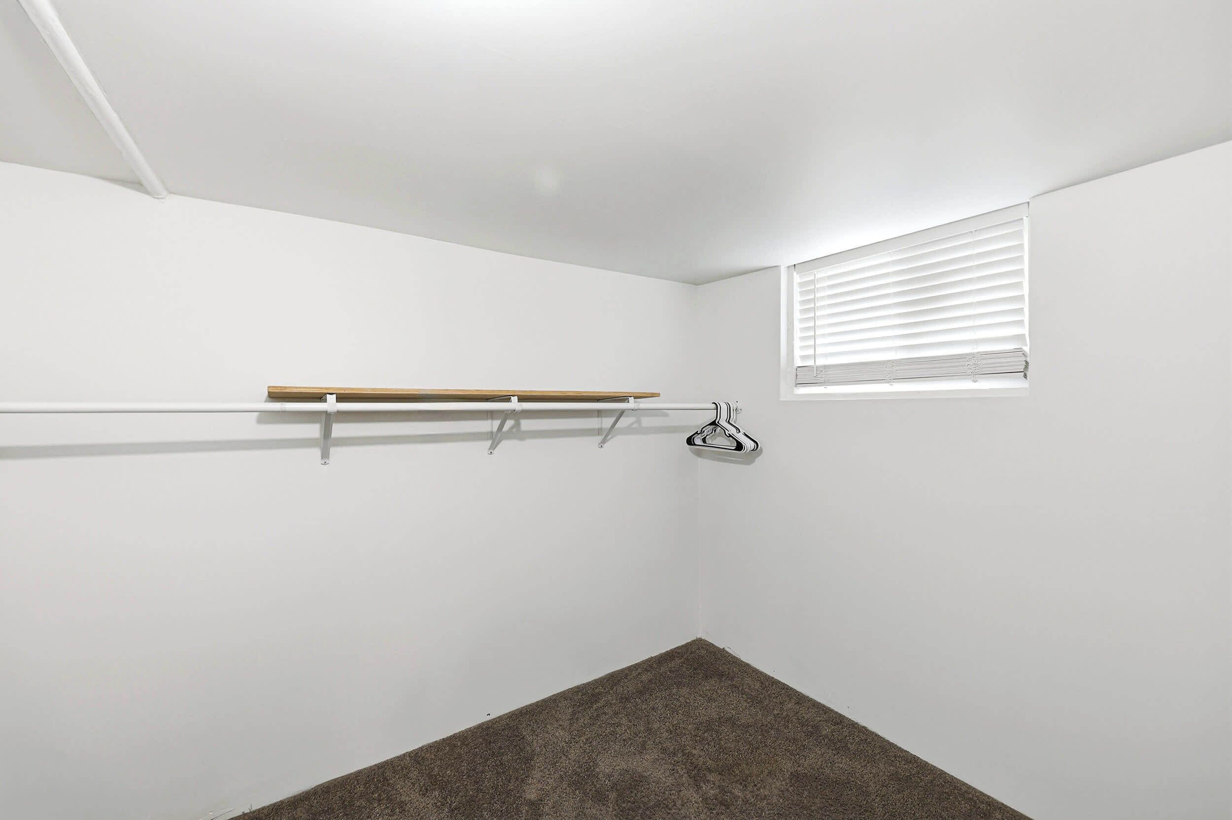 Una stanza con soffitto bianco, una finestra con persiane, uno scaffale di legno e un appendiabiti.