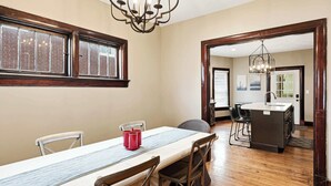 Uma sala de jantar com uma mesa comprida, cadeiras, um candelabro e vista para a cozinha.