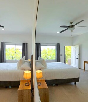 Quarto de hotel com duas camas, um ventilador de teto, uma janela grande com cortinas e uma porta que dá para o exterior.