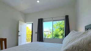 A bedroom with a large bed, a window with curtains, a door, and a ceiling fan. - Shared Pool Oasis  Near Malecon  BBQ  Wi-Fi (La Paz)