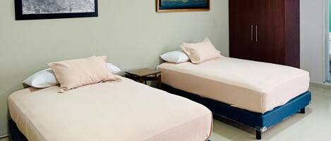 Two beds with blue frames, a wooden wardrobe, and two framed artworks on the wall.