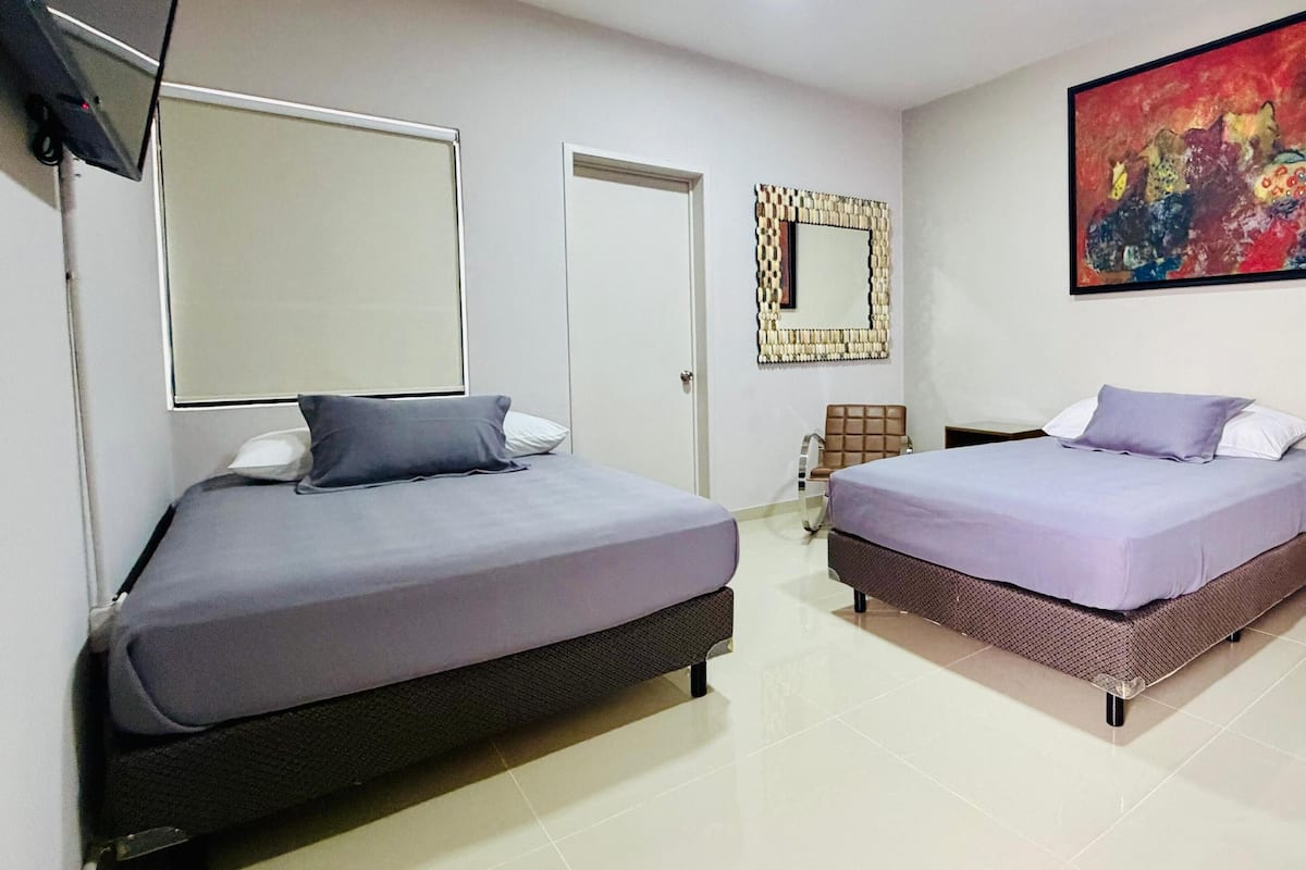 A hotel room with two beds, a TV, a mirror, a painting, and a nightstand with toiletries.