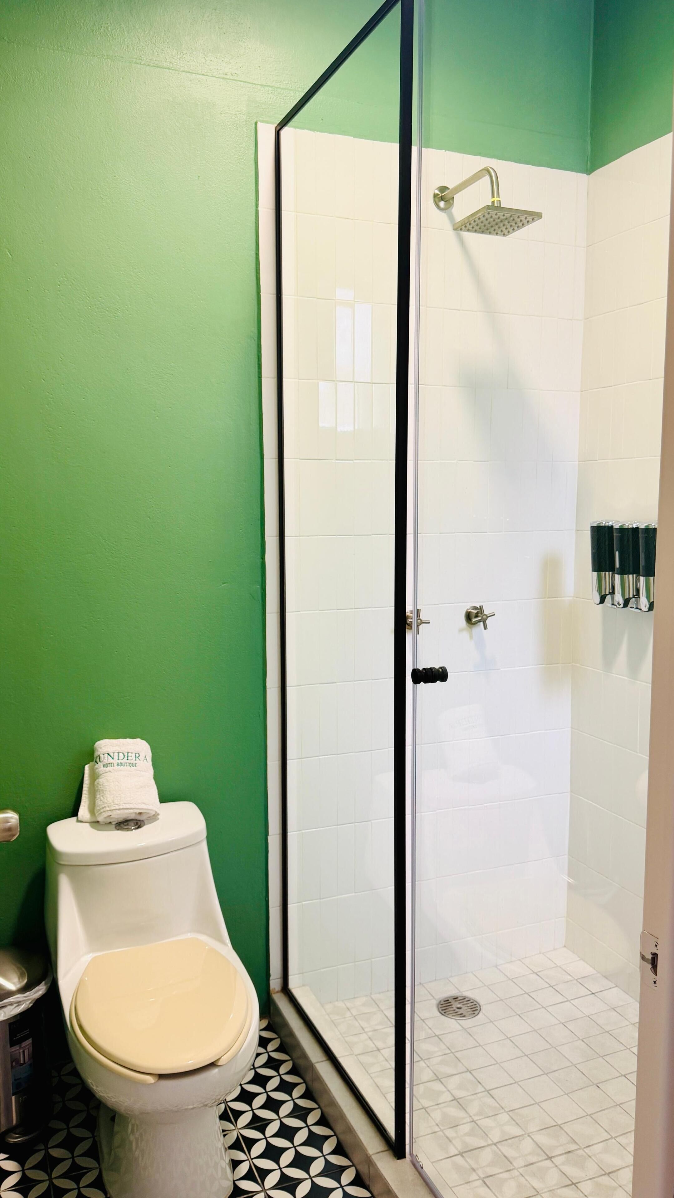 Un baño con inodoro, cabina de ducha y pared verde.