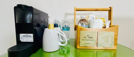A coffee maker, a white mug, a water bottle, a snack bar menu, and a wooden basket on a green table.