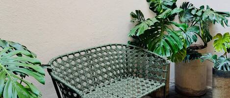A wicker chair in a courtyard with stone flooring and potted plants.