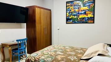 Une chambre à coucher avec un lit, un bureau, une chaise, une armoire et un tableau accroché au mur.