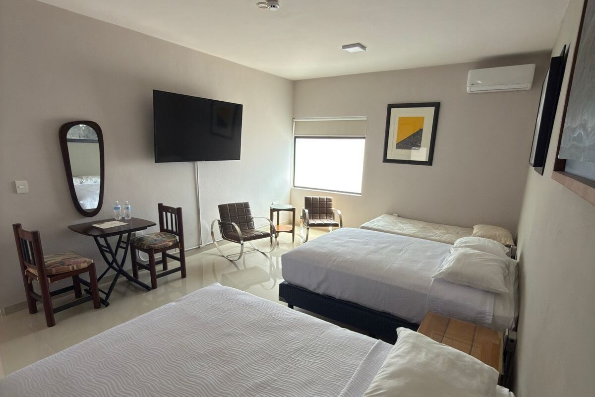 Une chambre d’hôtel avec deux lits, une télévision, un bureau avec des chaises et une fenêtre.