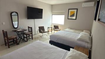 A hotel room with two beds, a TV, a desk with chairs, and a window.