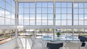 A balcony with a glass table and chairs, large windows, and a view of the cityscape. - Holiday Apartment 'Panoramic View Apartment' with Sea View, Wi-Fi and Air Conditioning (Quarteira)