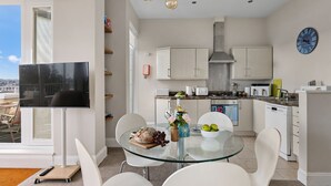 A modern kitchen with white cabinets, a glass dining table, and a view through the window. - Beach View Suite - Sea view, Balcony, Wi-fi (Torquay)