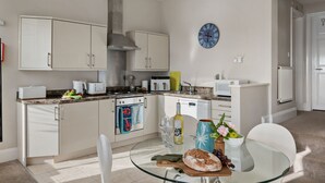 A modern kitchen with white cabinets, a stainless steel range hood, a clock, and a dining area with a glass table. - Beach View Suite - Sea view, Balcony, Wi-fi (Torquay)