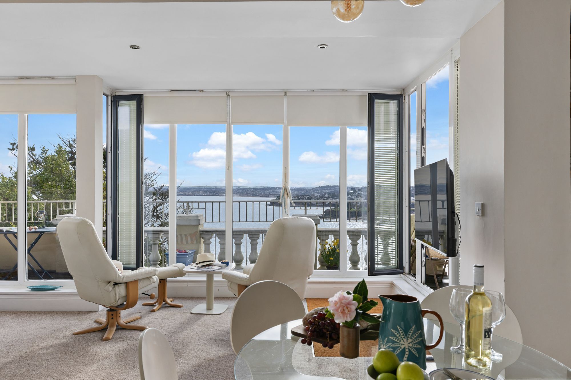 Un salon moderne avec une grande fenêtre, une table à manger et deux fauteuils blancs.