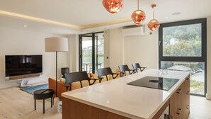 A modern kitchen with a central island, a dining area with chairs, a TV, and a large window with a view. - 4 The Reach - Pool & Spa facilities,  Sea views, Pet friendly (Salcombe)