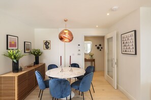 A modern dining area with a round table, blue chairs, a copper pendant light, and artwork on the walls. - 4 The Reach - Pool & Spa facilities, Sea views, Pet friendly (Salcombe)