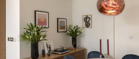 A modern dining area with a round marble table, blue chairs, a wooden sideboard, and two potted plants.