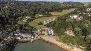 An aerial view of a coastal area with a large building complex, a sandy beach, and surrounding greenery. - 4 The Reach - Pool & Spa facilities,  Sea views, Pet friendly (Salcombe)