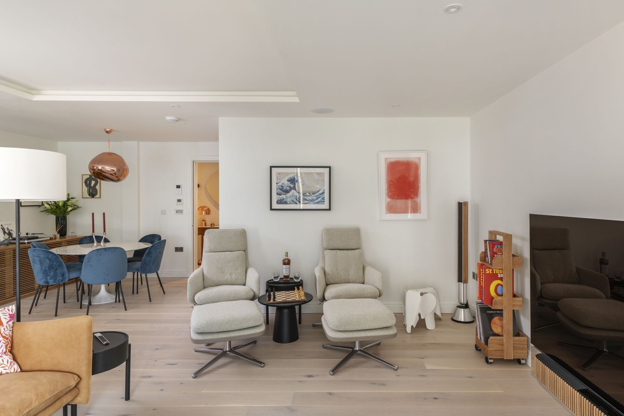 A modern living room with two armchairs, a dining area, a TV, and a bookshelf.