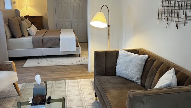 Ein modernes Wohnzimmer mit Sofa, Couchtisch, Lampe und einem Bett im Hintergrund.