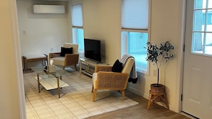 Ein Wohnzimmer mit Glastisch, Korbstühlen, Fernseher und einer Topfpflanze.