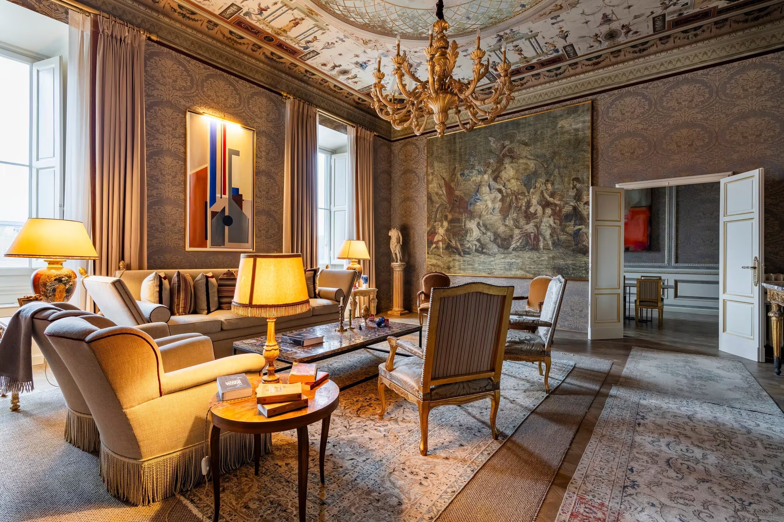 Un salón amplio con una gran araña, un cuadro de gran tamaño y vistas al comedor.