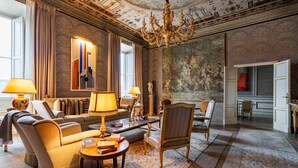 Un salón amplio con una gran araña, un cuadro de gran tamaño y vistas al comedor.
