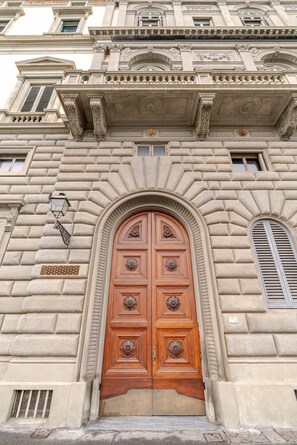A large, ornate wooden door with intricate carvings, set within a classical architectural style building facade. - Palazzo Angelico: Luxury Apartment on the Lungarno (Firenze)
