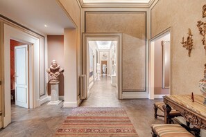 A hallway with a patterned rug, a bust sculpture, and a mirror with ornate details. - Palazzo Angelico: Luxury Apartment on the Lungarno (Firenze)