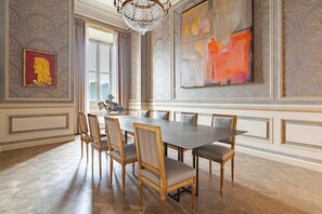Une salle à manger avec une grande table et six chaises, un lustre et deux grandes peintures accrochées aux murs.