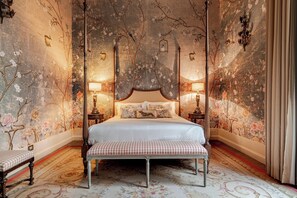 Une chambre à coucher avec un lit à baldaquin, un papier peint à motifs floraux et un banc.