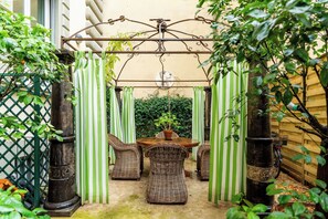 A covered patio area with a table and wicker chairs, surrounded by green-striped curtains and a metal trellis overhead. - Palazzo Angelico: Luxury Apartment on the Lungarno (Firenze)