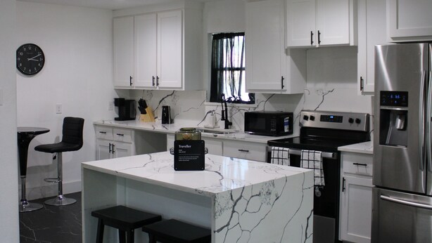 A modern kitchen with white cabinets, a marble island, black stools, and stainless steel appliances. - Up Up And Stayyyyy at this 3 bdrm Contemporary Home (Dallas)