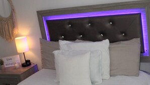 A neatly made bed with a headboard featuring a tufted design and a purple light strip. - Up Up And Stayyyyy at this 3 bdrm Contemporary Home (Dallas)