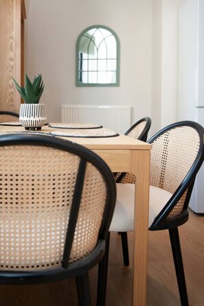 A dining area with a wooden table and rattan chairs, a potted plant, and a window with a green frame. - Fresh and spacious 3 bedroom home (Angus)