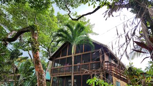 A wooden two-story building surrounded by lush tropical vegetation. - Sandy Bay Island Retreat w/Private Dock, Reef Snorkeling, Pool & Walk to Beach (Roatán)