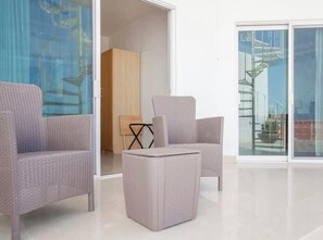 Ein modernes Interieur mit Korbmöbeln, einer Glastür, die auf einen Balkon führt, und einer dahinter liegenden Wendeltreppe.