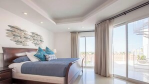 Ein Schlafzimmer mit einem großen Bett, einem Nachttisch, einer Wanddekoration und einem Balkon mit Vorhängen.