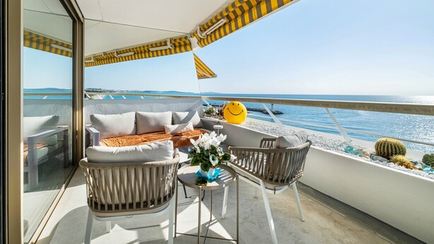A balcony with a sofa, chairs, and a table with a vase of flowers. - Apartment 'Grand Luxe Vue Mer Exclusif' with Sea View, Wi-Fi and Air Conditioning (Villeneuve-Loubet)