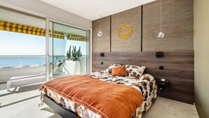 A bedroom with a bed, a view of the sea, a balcony, and a wooden wall with a circular decoration. - Apartment 'Grand Luxe Vue Mer Exclusif' with Sea View, Wi-Fi and Air Conditioning (Villeneuve-Loubet)
