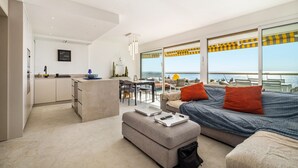 A modern living room with a sofa, ottoman, and dining area. - Apartment 'Grand Luxe Vue Mer Exclusif' with Sea View, Wi-Fi and Air Conditioning (Villeneuve-Loubet)