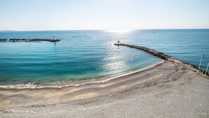 A coastal scene with a lighthouse, calm sea, and a pebbly beach. - Apartment 'Grand Luxe Vue Mer Exclusif' with Sea View, Wi-Fi and Air Conditioning (Villeneuve-Loubet)