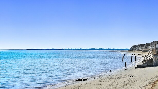 A beach with a clear sky, a sandy shore, and a row of buildings along the water.