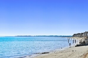 Una playa con cielo despejado, una orilla arenosa y una hilera de edificios a lo largo del agua.