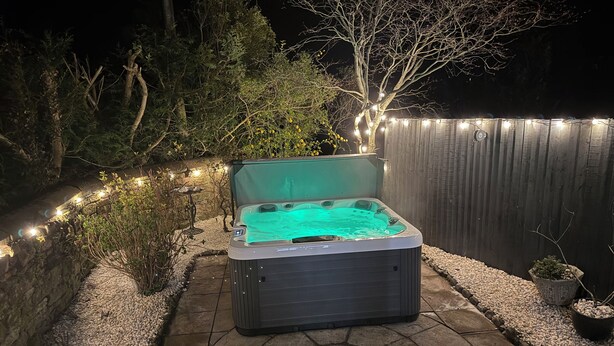 A hot tub in a backyard with a stone pathway, surrounded by plants and a wooden fence. - Broadwath Old House (Brampton)