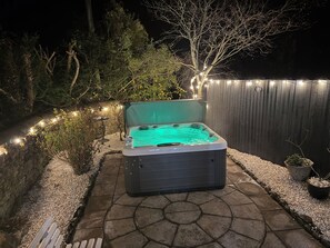 A hot tub in a backyard with a stone pathway, surrounded by plants and a wooden fence. - Broadwath Old House (Brampton)