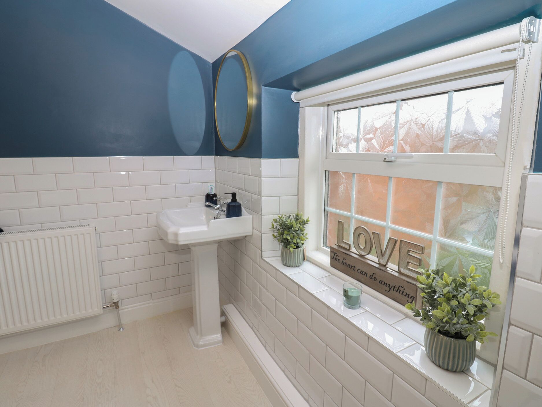 Un bagno con un lavandino bianco, una finestra con la scritta 'LOVE' e un termosifone.