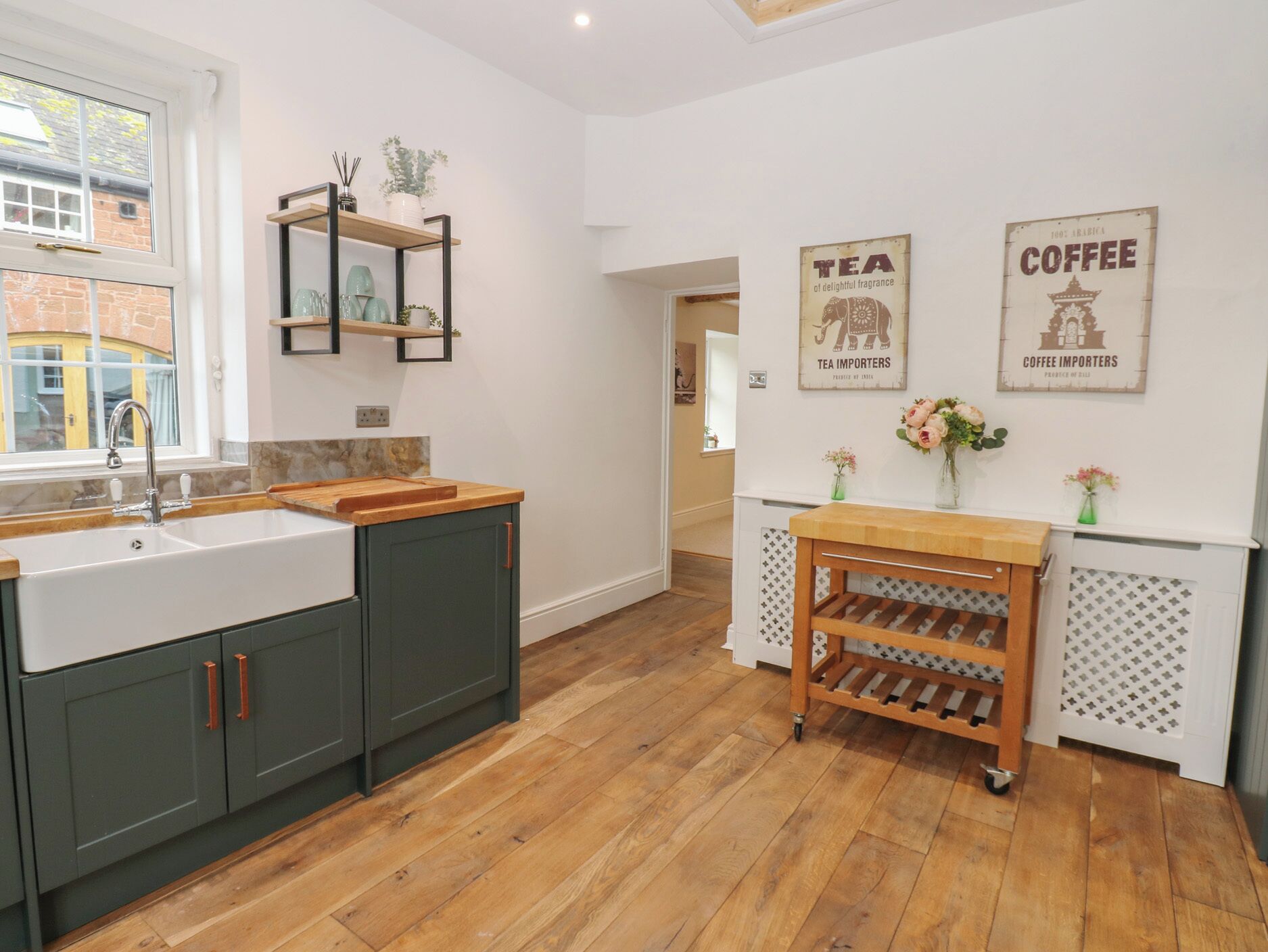 A modern kitchen with a sink, cabinets, a wooden countertop, a shelf with decorative items, and wall-mounted signs.